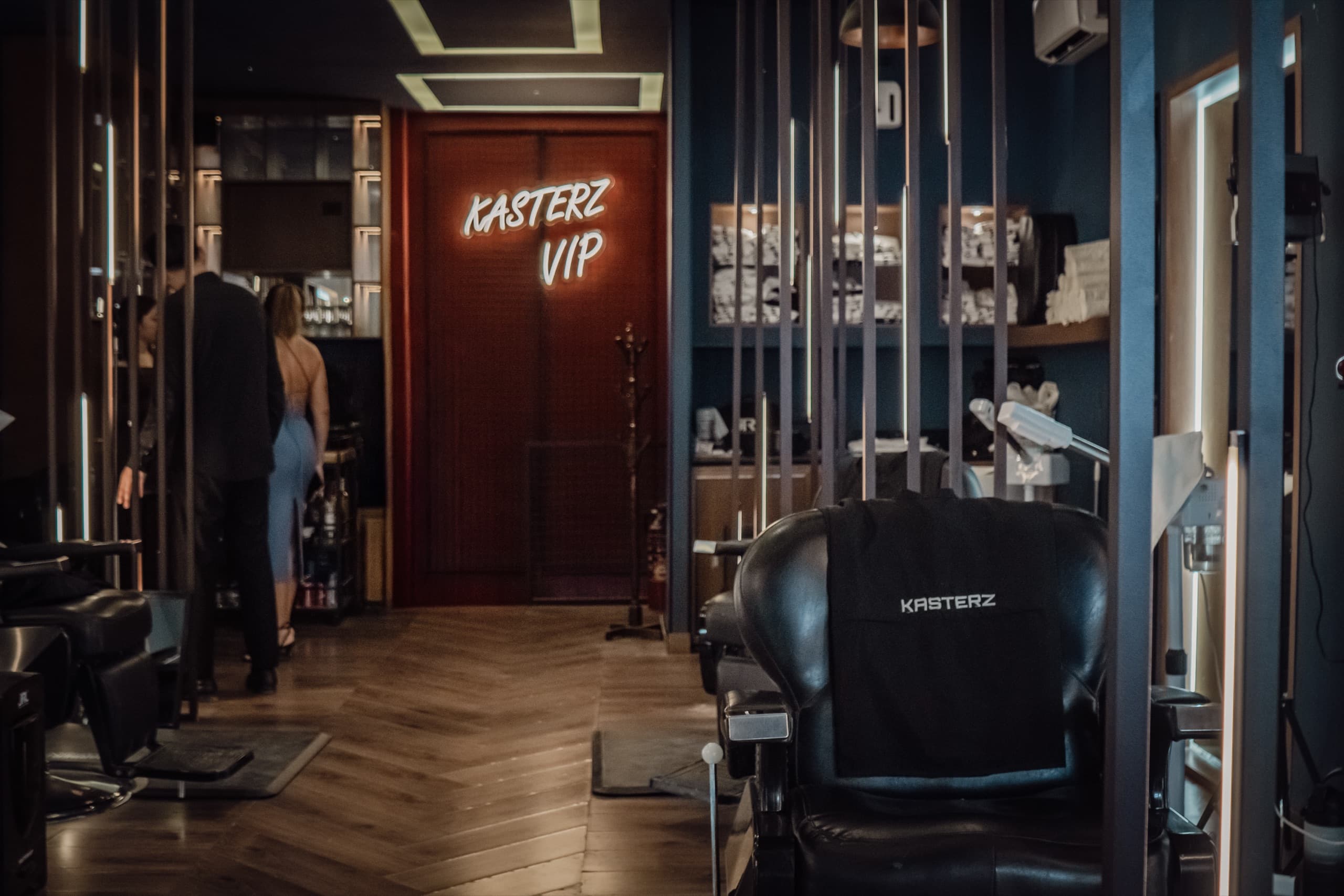 Interior del club Kasterz: sillón de barbero con capa de marca y letrero de neón KASTERZ VIP al fondo